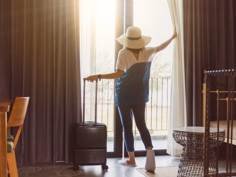 Asian women are staying in a hotel room with luggage.Open the curtain and  door in the room looking to outside view.Travel in holidays concept.Vintage tone.